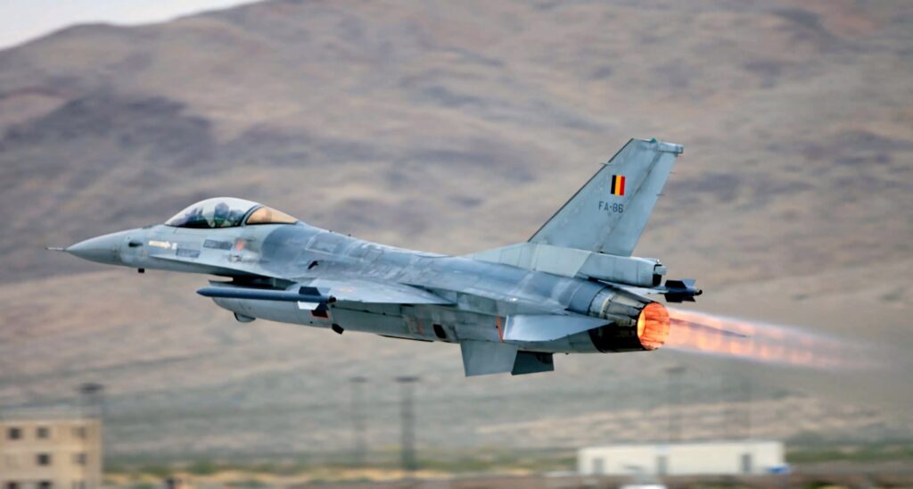 General Dynamics F-16 Fighting Falcon jet with blazing afterburner flying over arid mountains Wallpaper