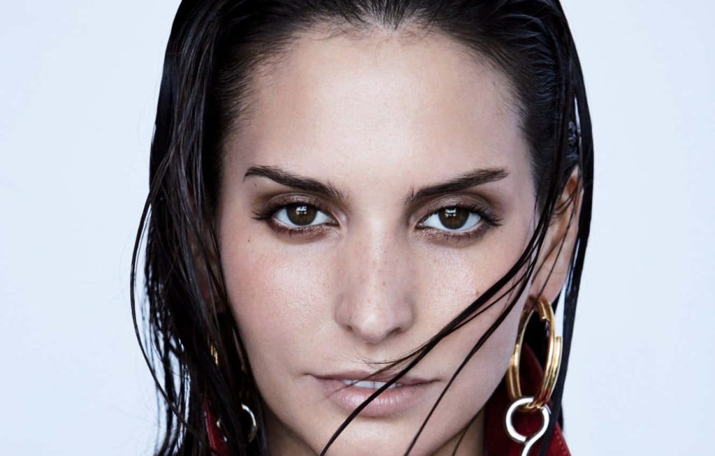 Close-up portrait of Genesis Rodriguez with wet-look hair and gold hoop earrings white background Wallpaper