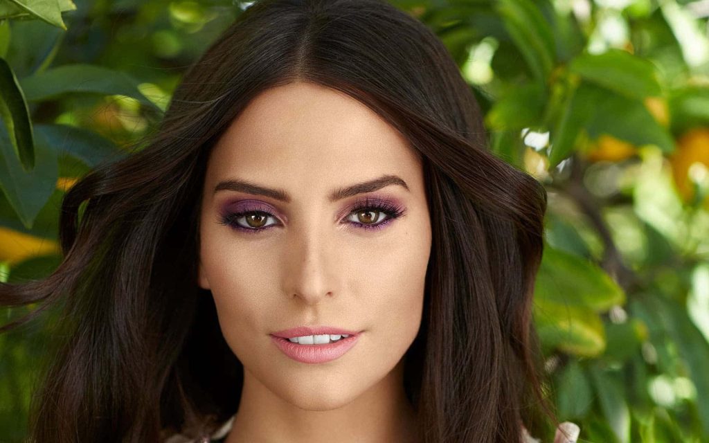 Close up portrait of Genesis Rodriguez with purple eyeshadow and green foliage background wallpaper