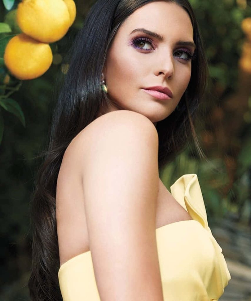 Portrait of Genesis Rodriguez in yellow top with soft-focus citrus tree background vibrant wallpaper