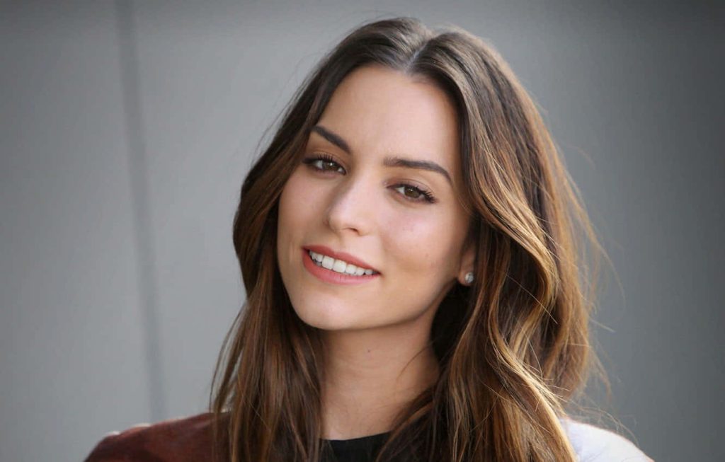 Portrait of Genesis Rodriguez with warm smile and flowing brown hair in soft studio light Wallpaper