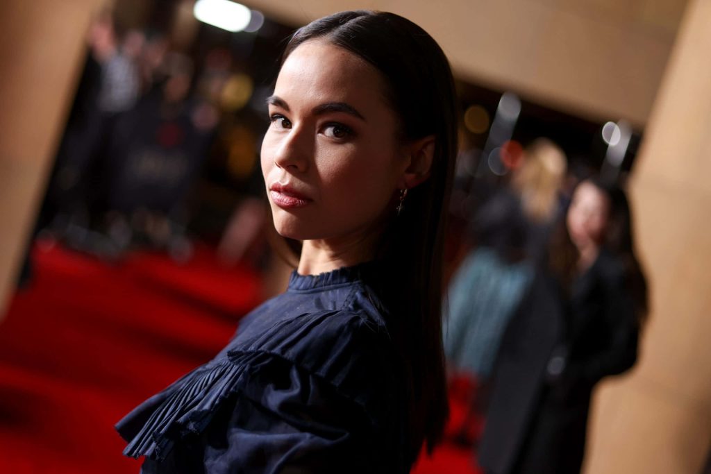 Actress Genevieve Kang poses gracefully in a dark ruffled top on red carpet with cinematic lighting Wallpaper