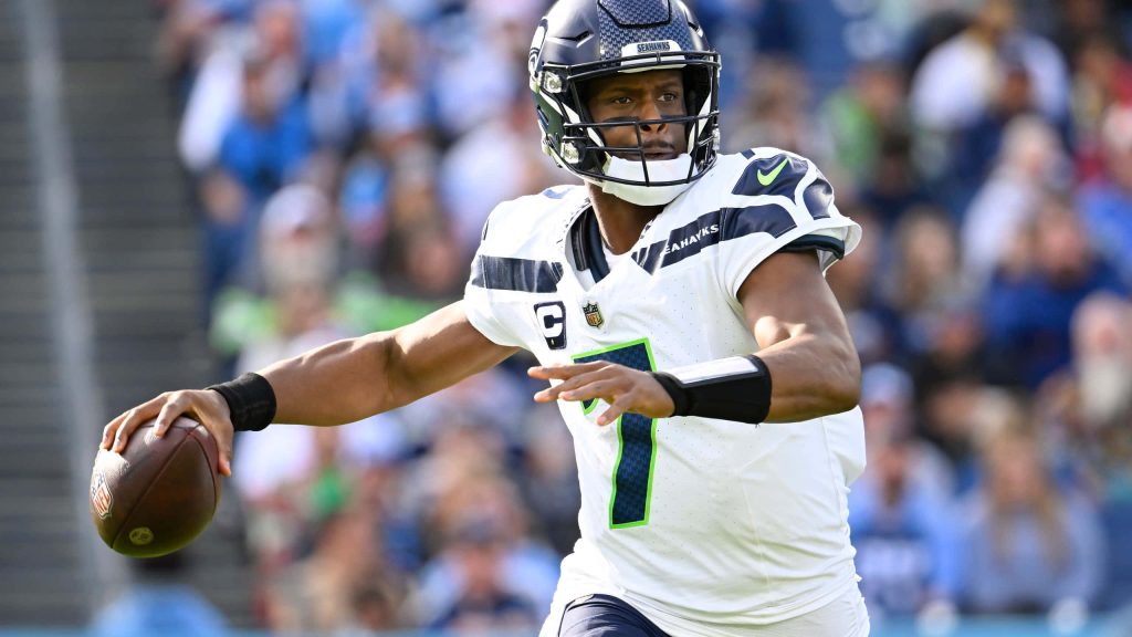 NFL quarterback Geno Smith in white uniform ready to pass on field with blurred stadium background Wallpaper