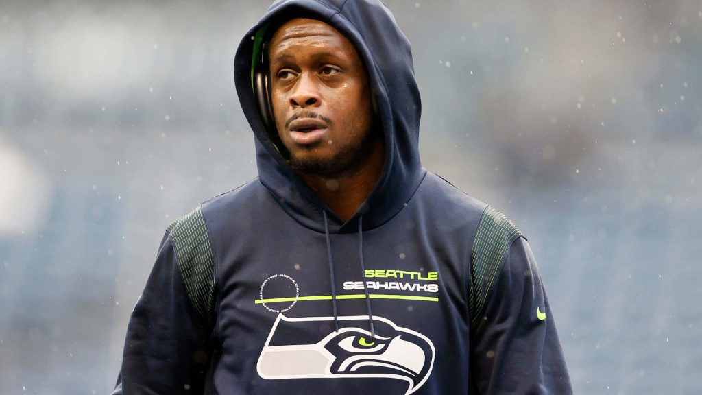 NFL quarterback Geno Smith focused in navy Seahawks hoodie rain intense sports wallpaper background