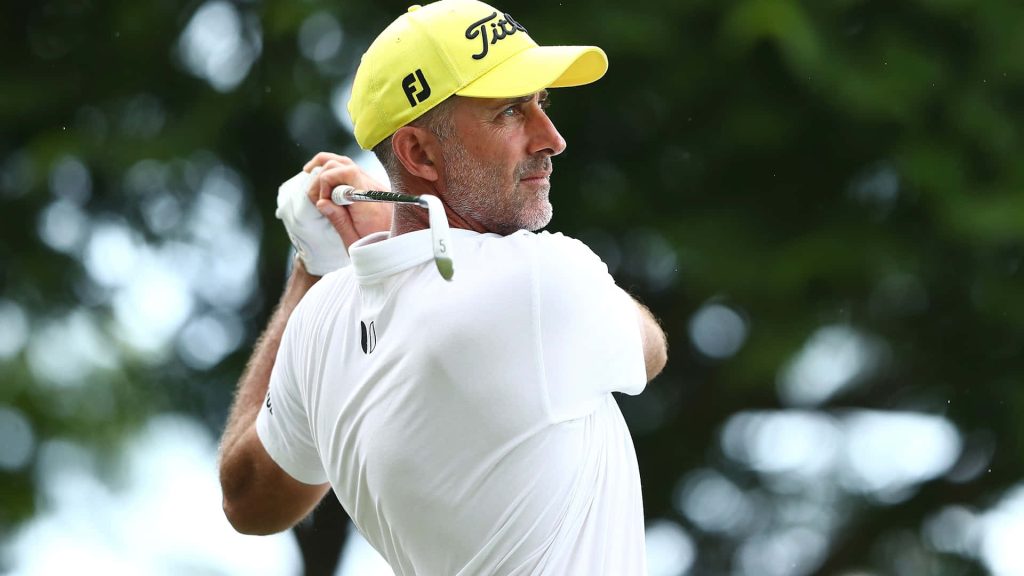 Professional golfer Geoff Ogilvy mid-swing wearing yellow cap and white polo on green golf course Wallpaper