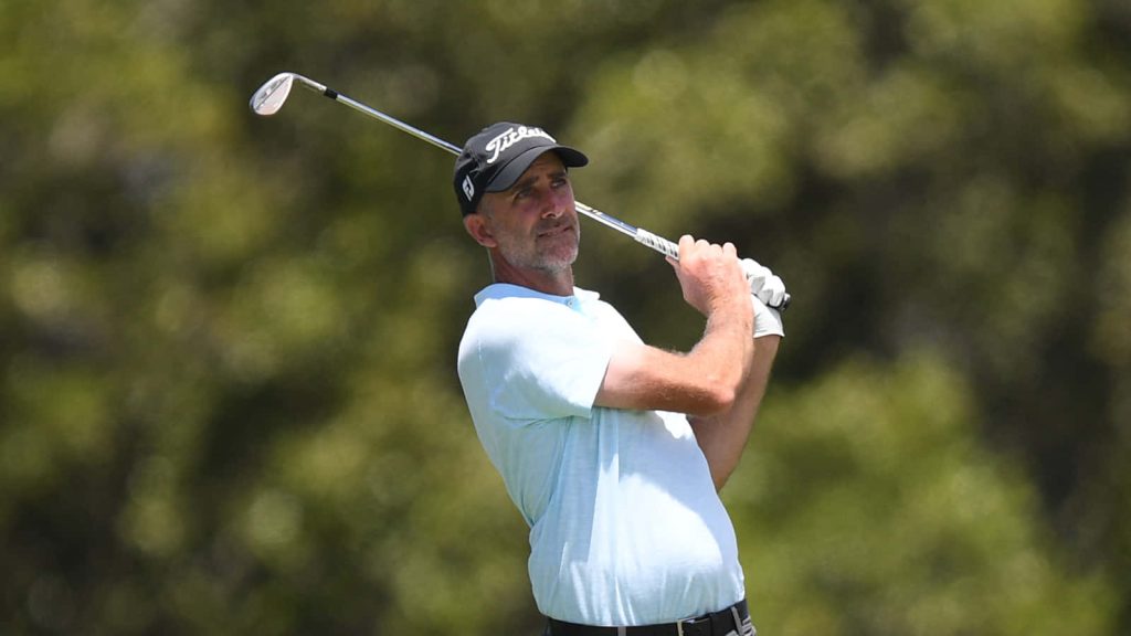 Geoff Ogilvy golf swing follow-through in light blue polo and Titleist cap on blurred course Wallpaper