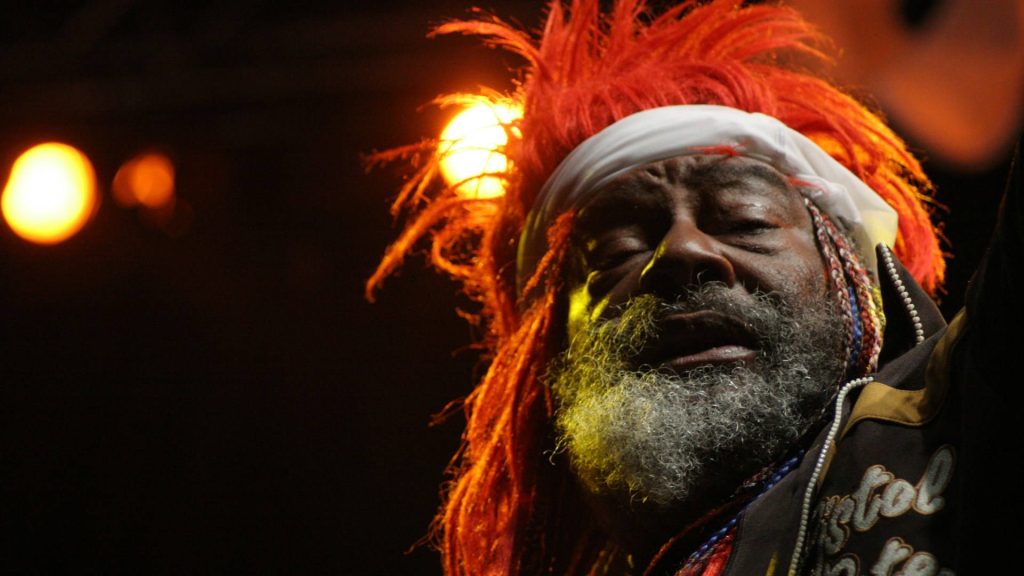 George Clinton dynamic concert portrait vibrant red hair expressive gray beard stage lighting Wallpaper