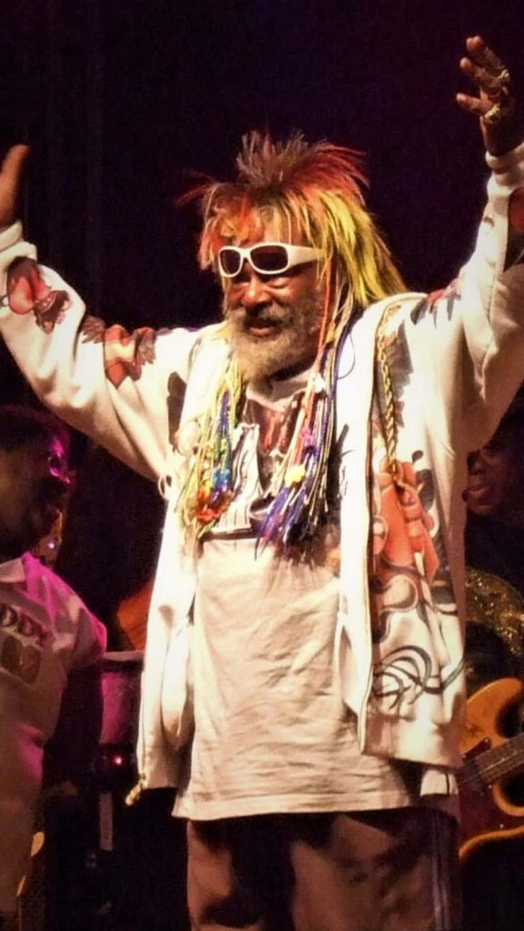 George Clinton live concert vibrant wallpaper with colorful hair white sunglasses and graphic jacket