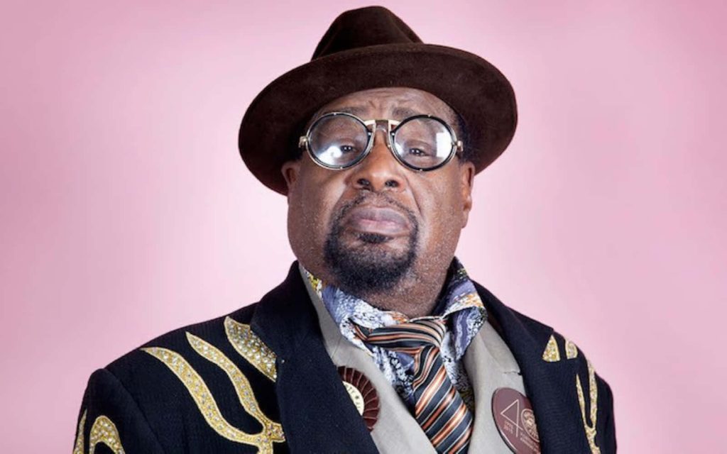 Studio portrait of George Clinton in fedora glittery coat pink background iconic funk legend Wallpaper