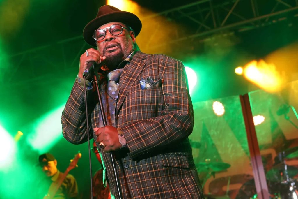 George Clinton performing live in fedora and plaid blazer under vibrant green and gold lights Wallpaper