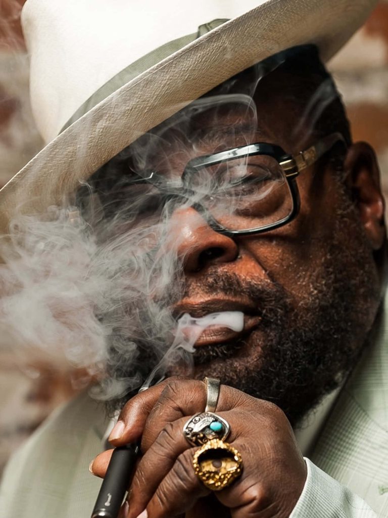 George Clinton portrait wallpaper iconic musician fedora glasses rings dramatic smoke background