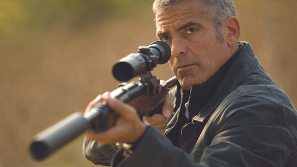 George Clooney aiming rifle with intense focus in dramatic scene from The American film outdoors Wallpaper