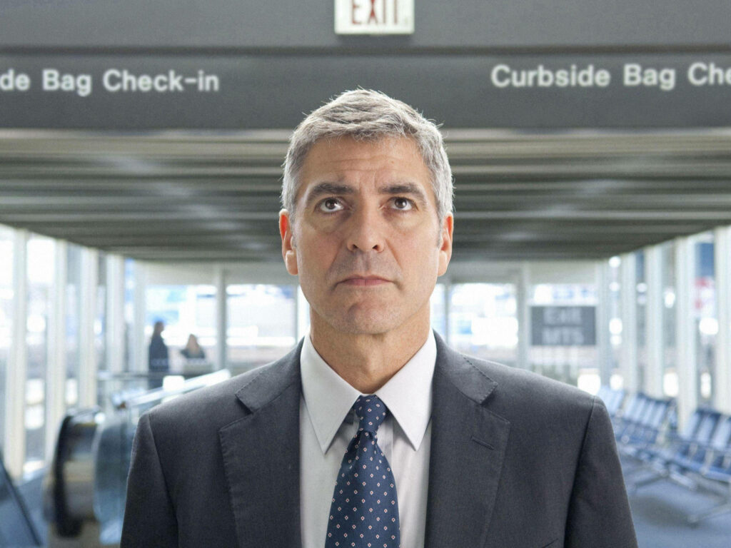 George Clooney in airport terminal near exit passage wearing suit with curbside bag check-in sign Wallpaper
