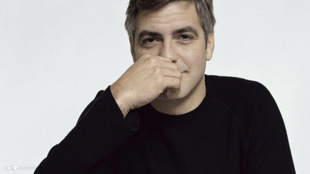 George Clooney in black sweater with subtle smile hand on face plain light background wallpaper