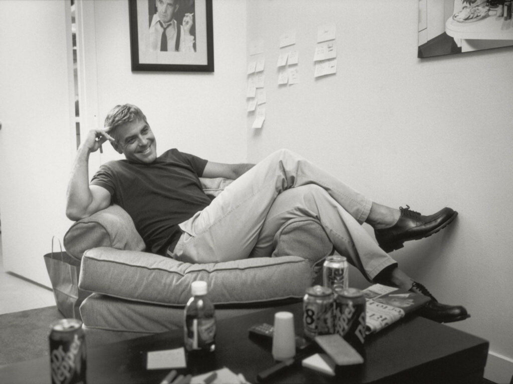 George Clooney relaxing on modern couch with drinks and notes in casual black and white setting Wallpaper