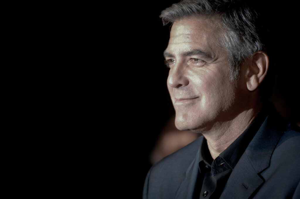 Side view of George Clooney in dark suit softly lit against black background wallpaper