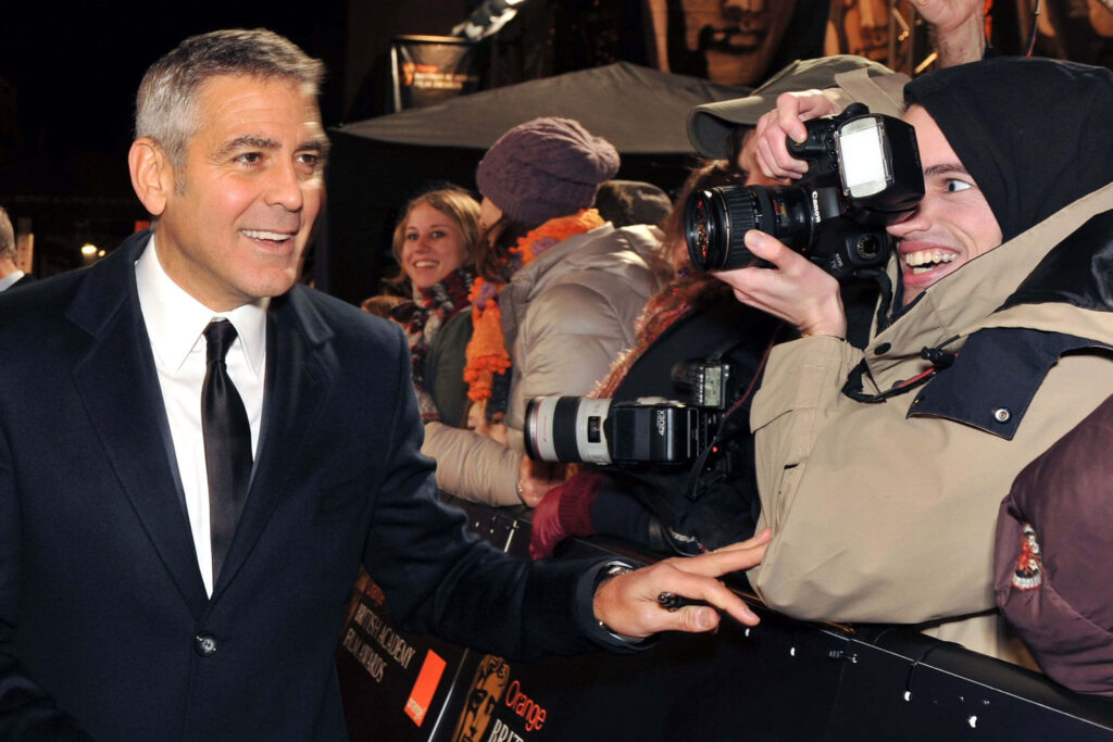 George Clooney smiling and engaging with fans on red carpet creating glamorous vibrant scene Wallpaper