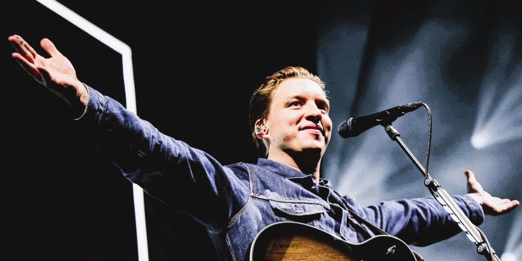 George Ezra performing live with acoustic guitar in denim shirt under dramatic stage lights Wallpaper