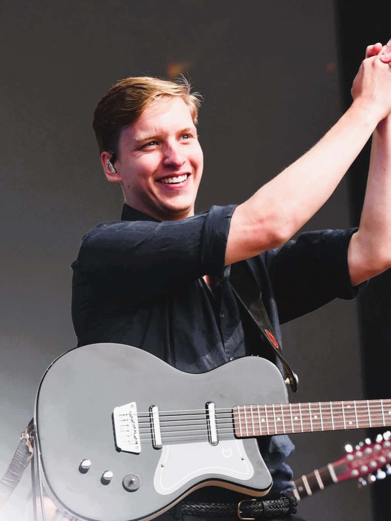 George Ezra smiling live on stage playing electric guitar vibrant concert wallpaper background