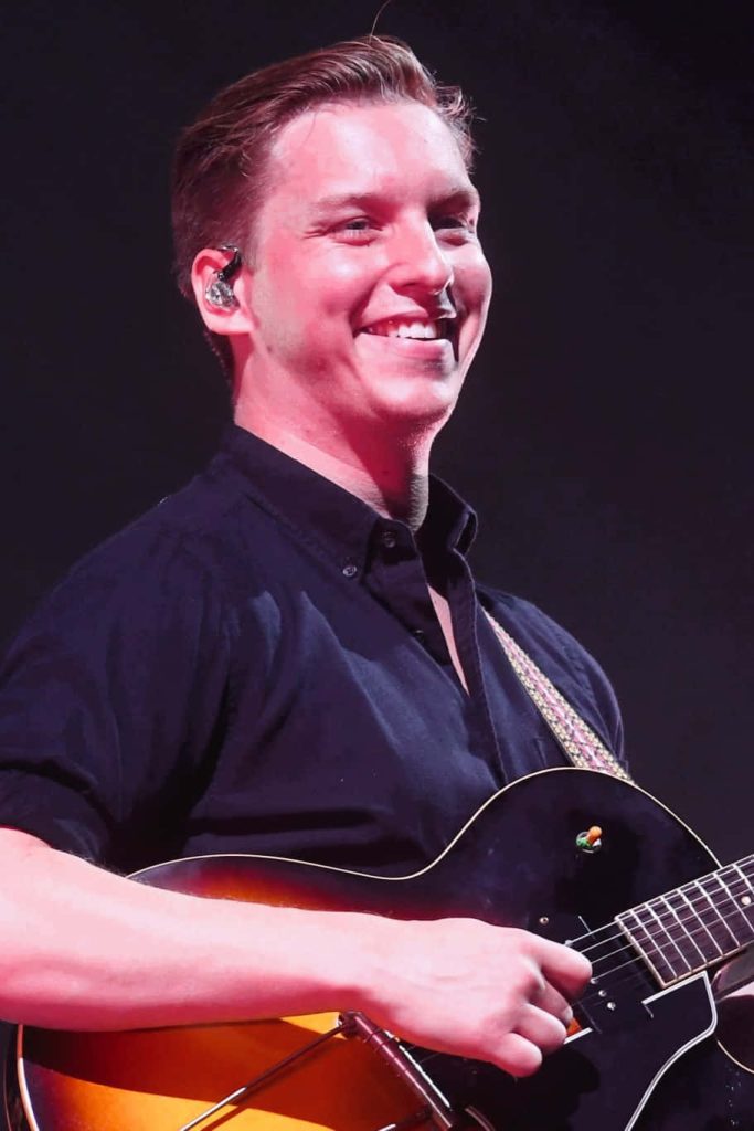 George Ezra live performance wallpaper singing and playing guitar with joyful energy dark background