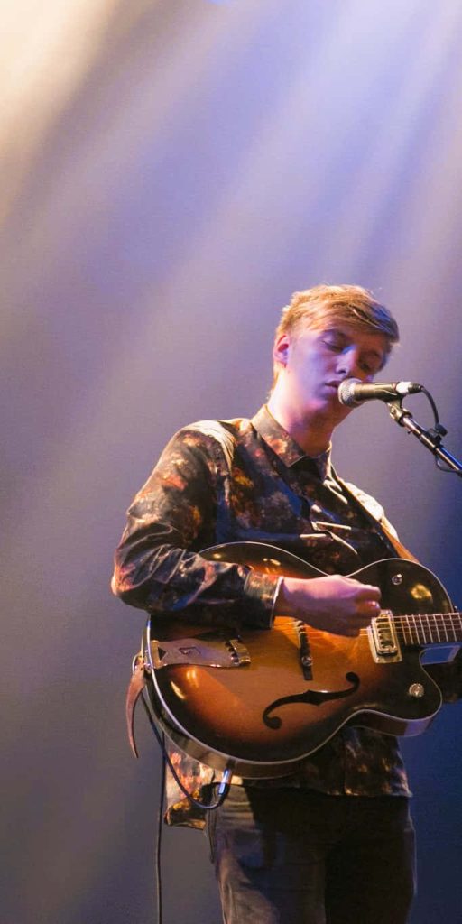 George Ezra live concert wallpaper playing hollow-body guitar in soft purple stage lighting