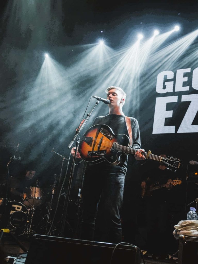 George Ezra live performance playing archtop guitar with dramatic stage lighting wallpaper