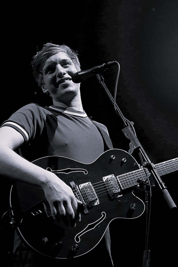 Black and white wallpaper of George Ezra smiling and playing electric guitar on stage live