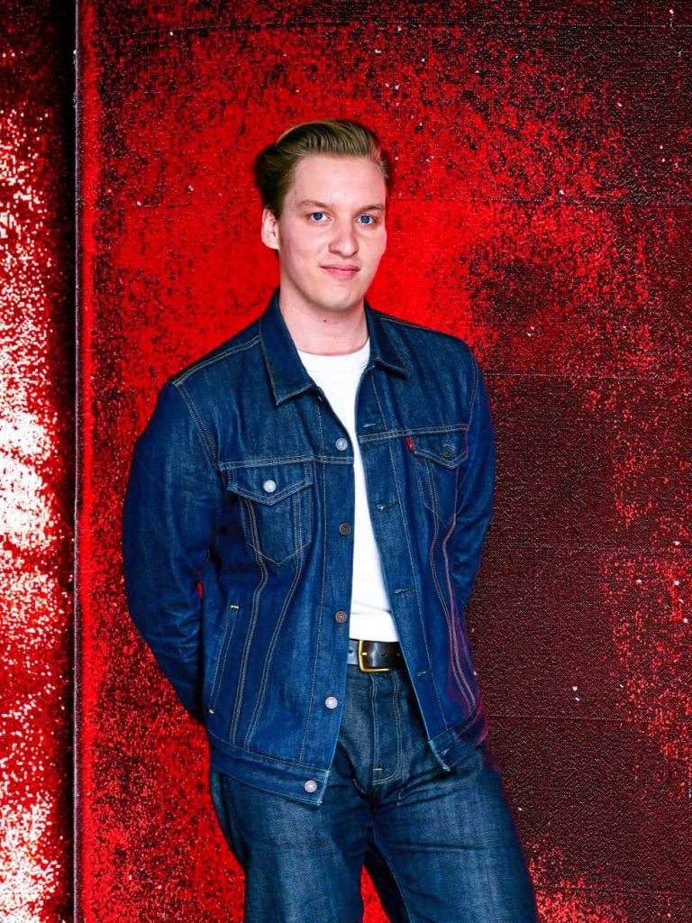 George Ezra portrait in dark denim jacket white tee red textured background vibrant wallpaper