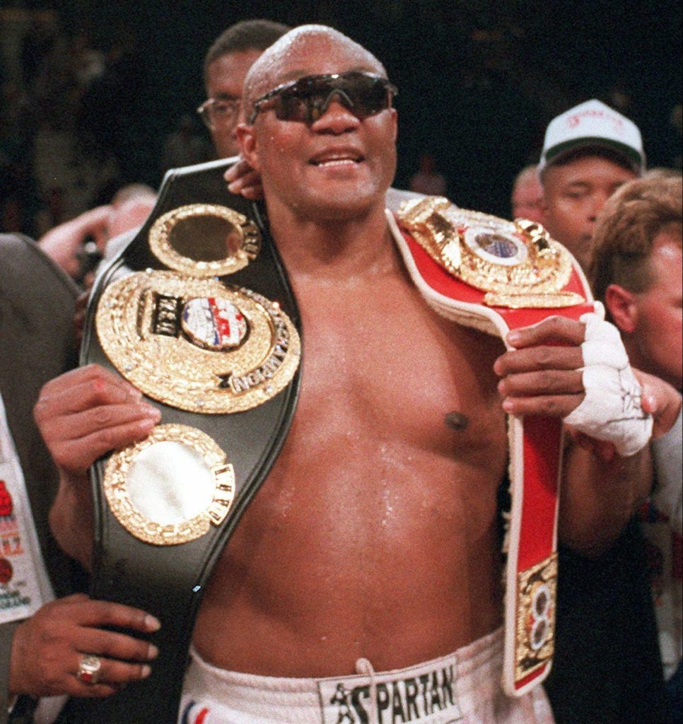 George Foreman triumphant in Spartan trunks with two heavyweight title belts high-resolution wallpaper