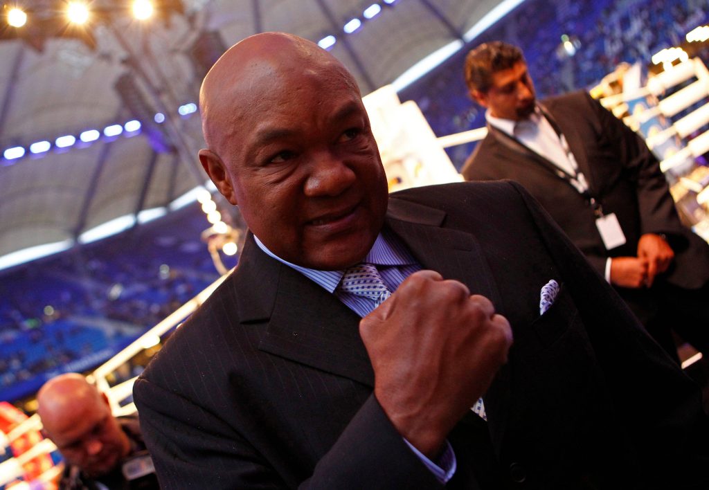 George Foreman in sharp suit raising fist smiling boxing arena background professional portrait Wallpaper
