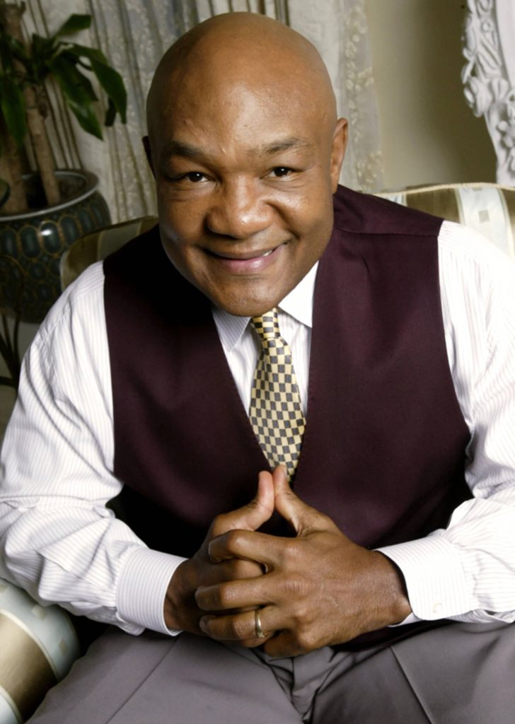 Portrait of boxing legend George Foreman in maroon vest smiling warmly professional wallpaperr