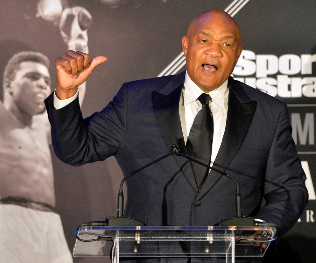 George Foreman speaking at press conference with Muhammad Ali backdrop in sharp suit Wallpaper
