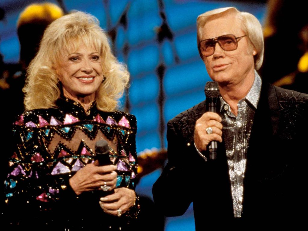 George Jones and Tammy Wynette singing live in colorful outfits on vibrant blue-lit stage wallpaper