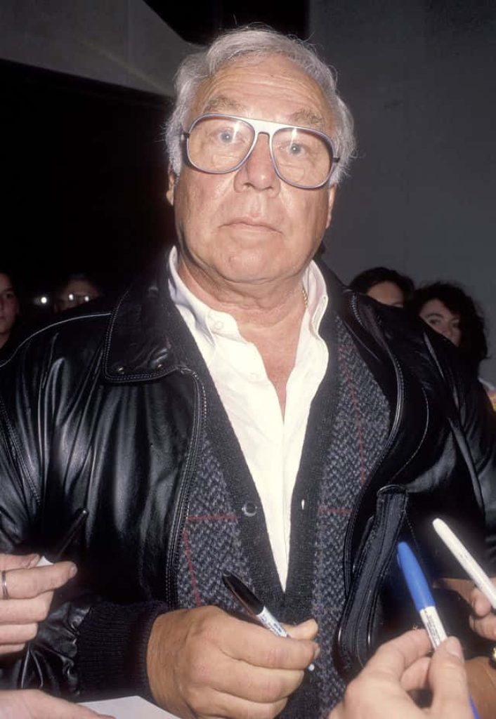 George Kennedy signing autographs in black leather jacket vintage glasses classic Hollywood wallpaper