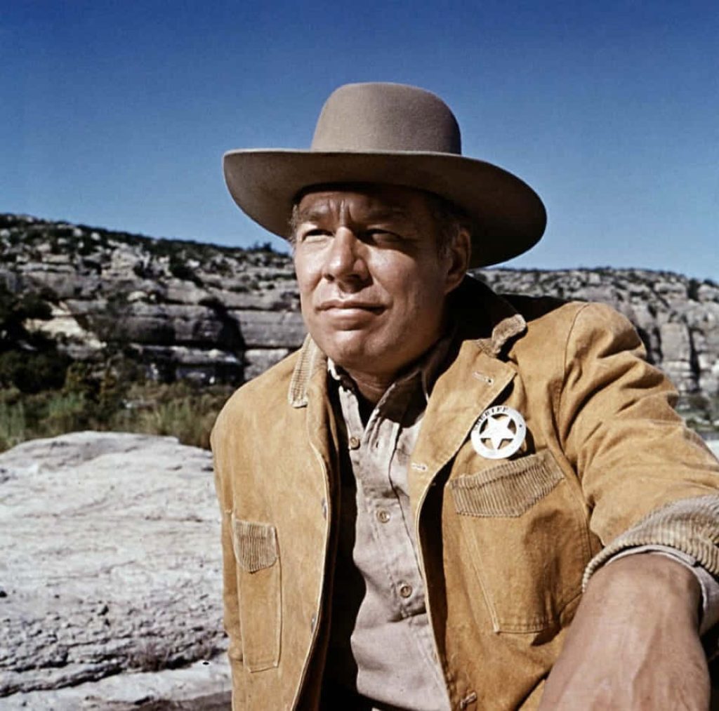 George Kennedy as Western sheriff in tan jacket star badge rugged sunlit rocky landscape wallpaper