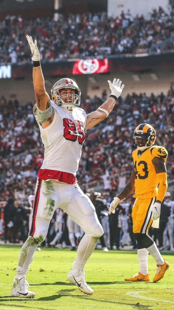 George Kittle in 49ers jersey celebrates big NFL play vibrant stadium background wallpaper