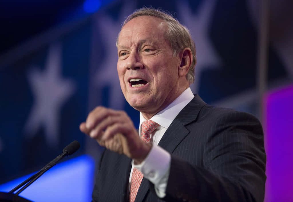 Former New York Governor George Pataki in dark suit delivering speech at podium patriotic backdrop Wallpaper