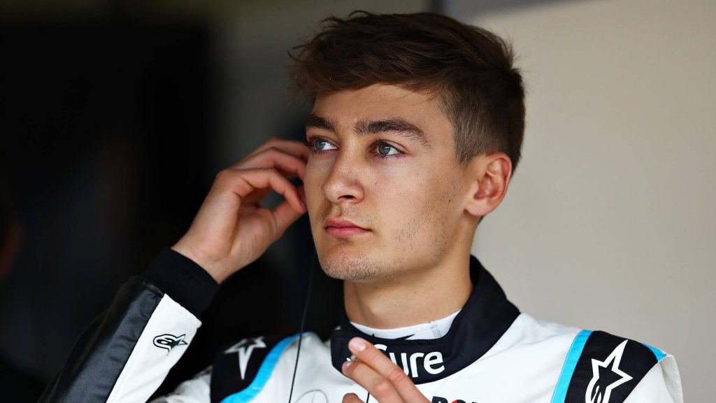 George Russell F1 driver portrait adjusting earpiece in racing suit with soft lighting background Wallpaper