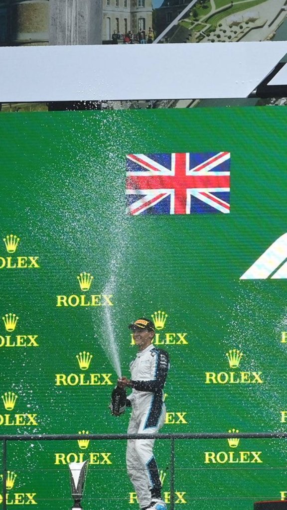 George Russell F1 victory celebration on podium with sparkling wine and British flag background Wallpaper