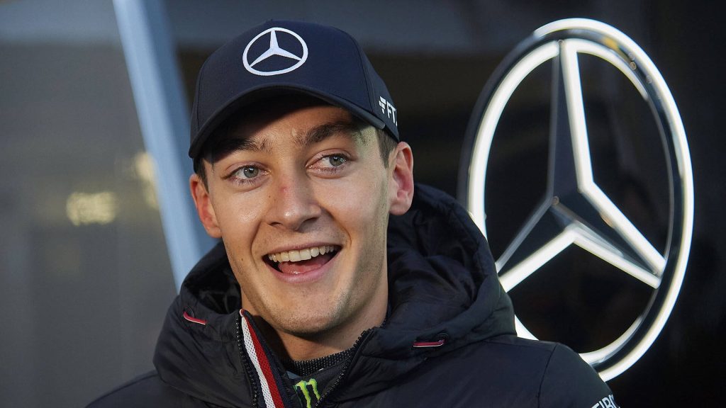 George Russell smiling in Mercedes F1 gear with glowing logo vibrant racing wallpaper background