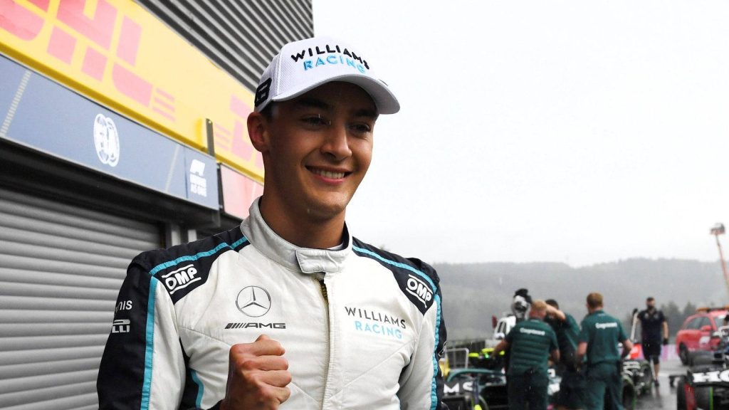 Formula 1 driver George Russell in white Williams Racing suit and cap smiling in F1 pit lane Wallpaper