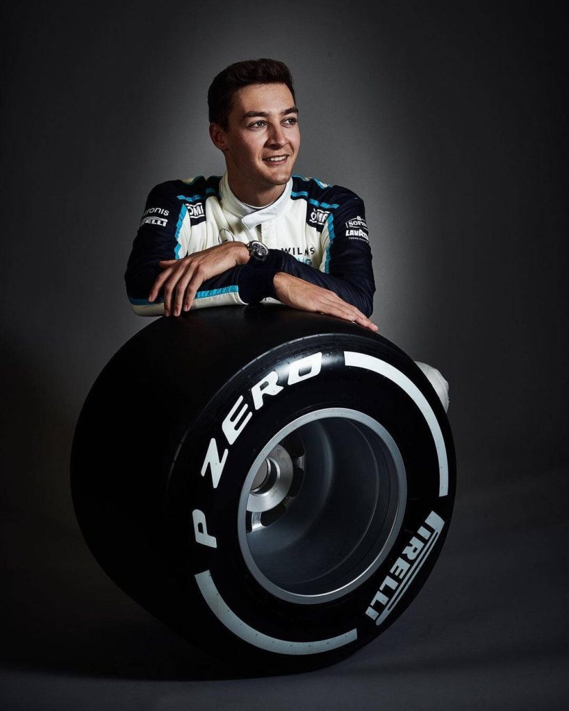 George Russell in Williams Racing suit leaning on large Pirelli P Zero tire studio portrait Wallpaper