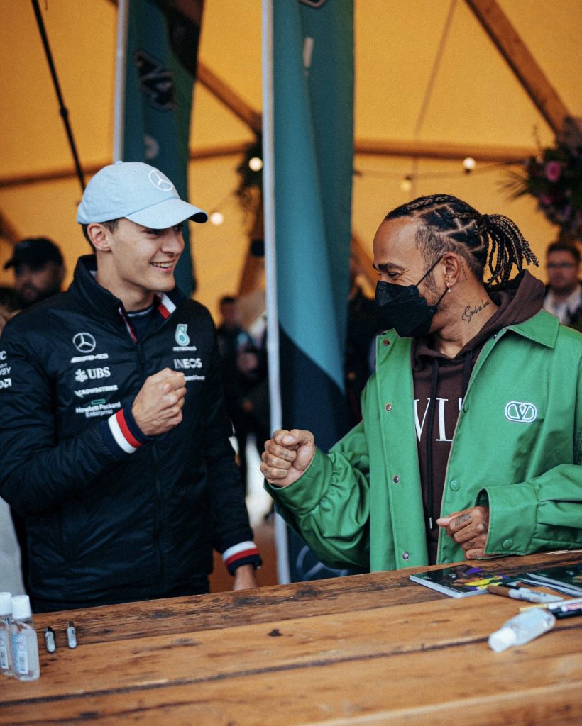 F1 teammates George Russell and Lewis Hamilton fist-bump trackside in warm glowing light wallpaper