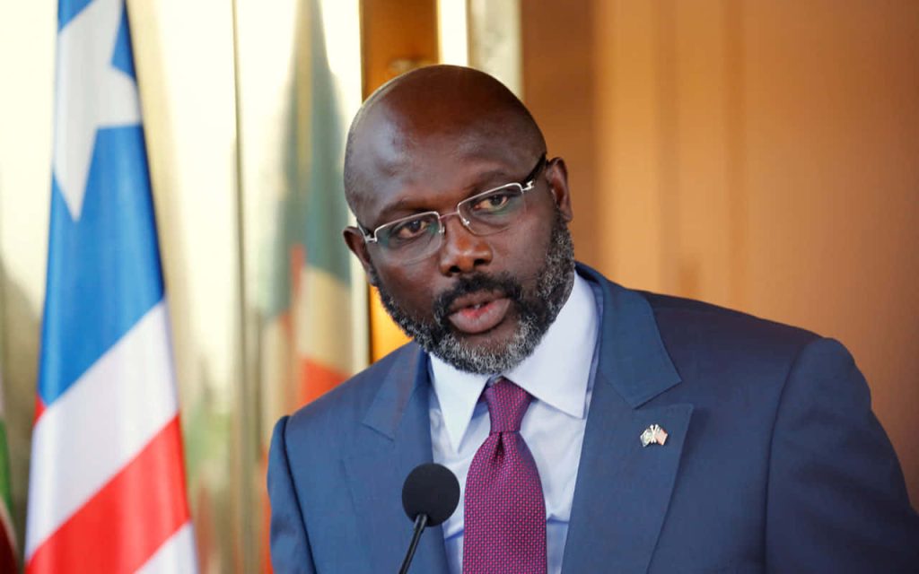 Former Liberian President George Weah delivering speech in suit with Liberian flag background Wallpaper