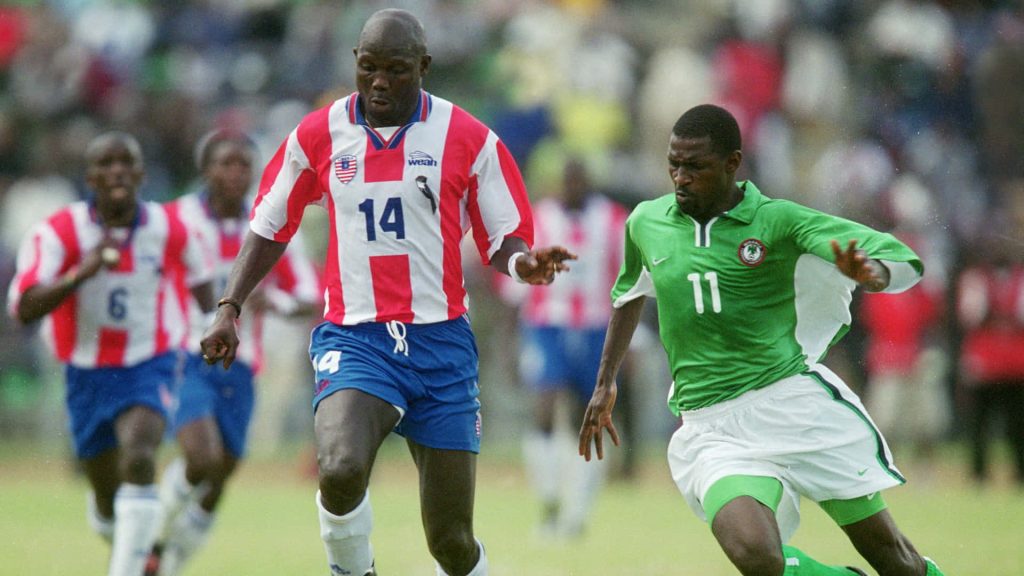 George Weah dribbling in Liberian red kit versus Nigerian player green jersey intense football action Wallpaper