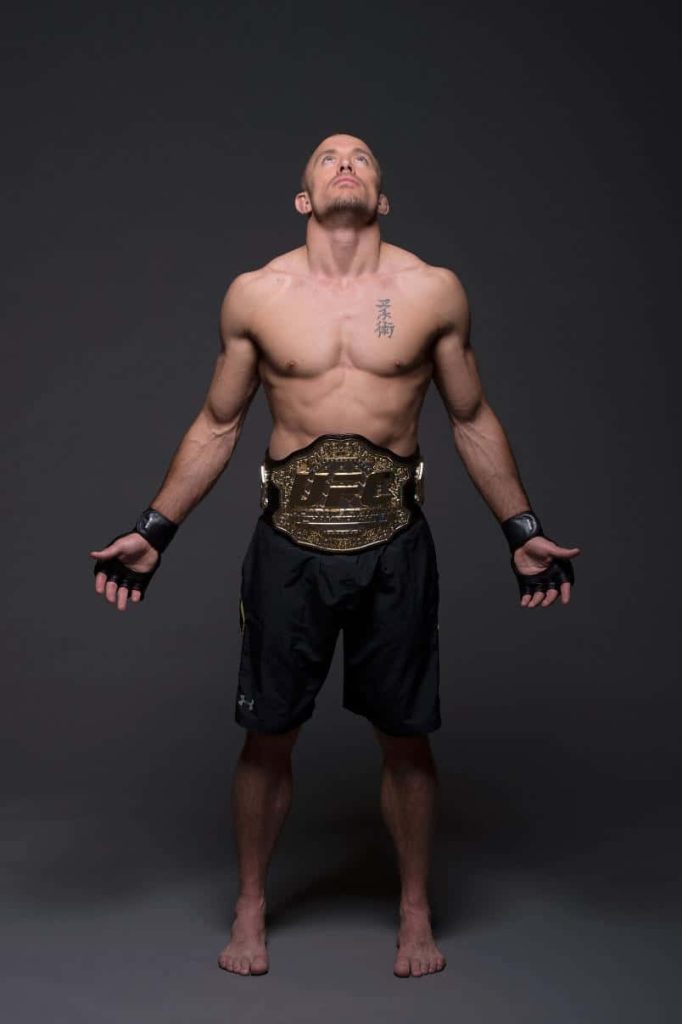 Georges St-Pierre shirtless with UFC belt and black gloves studio portrait dark grey background Wallpaper