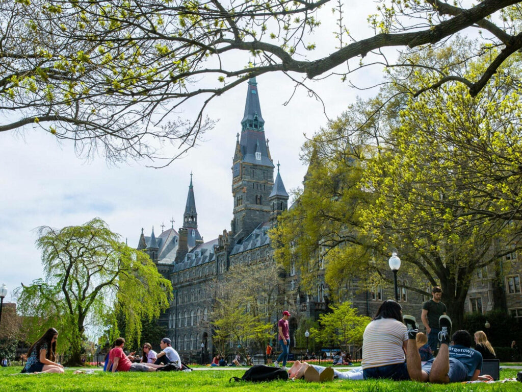 Students picnicking on Georgetown University lawns with Healy Hall spires under spring daylight Wallpaper