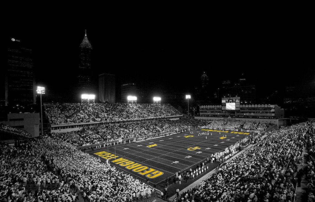 Black-and-white Georgia Tech Bobby Dodd Stadium packed crowd with yellow football field accents and Atlanta skyline Wallpaper
