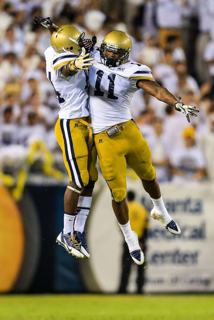 Georgia Tech Yellow Jackets mid-air chest bump in white gold jerseys under bright stadium lights Wallpaper
