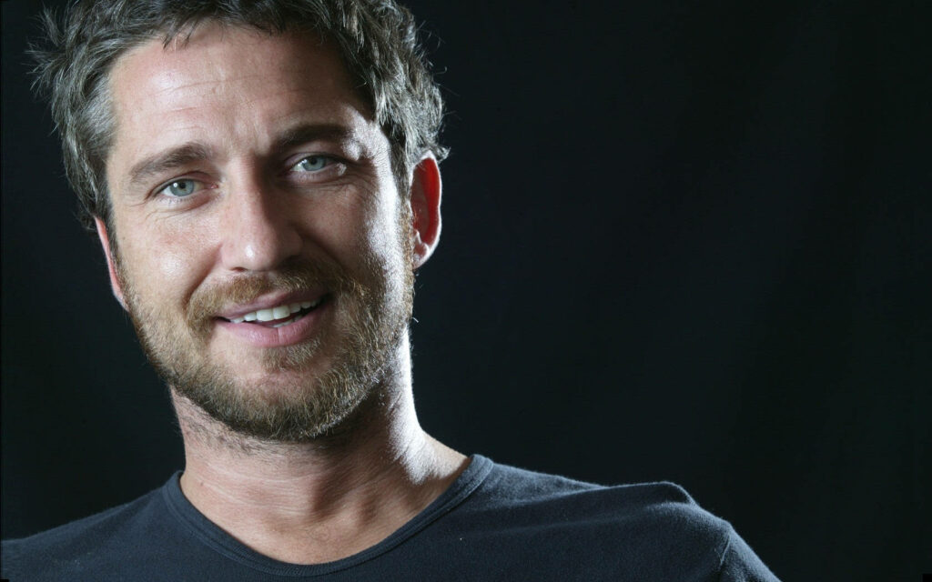 Scottish actor Gerard Butler smiling warmly with dark background for captivating wallpaper